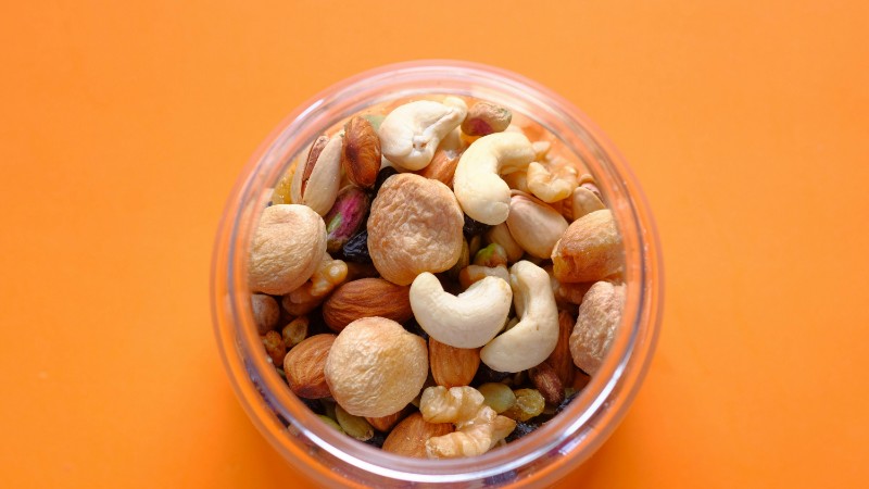 Close-up of a mix of nuts in a clear container against an orange background., tags: glutenfrei - pexel